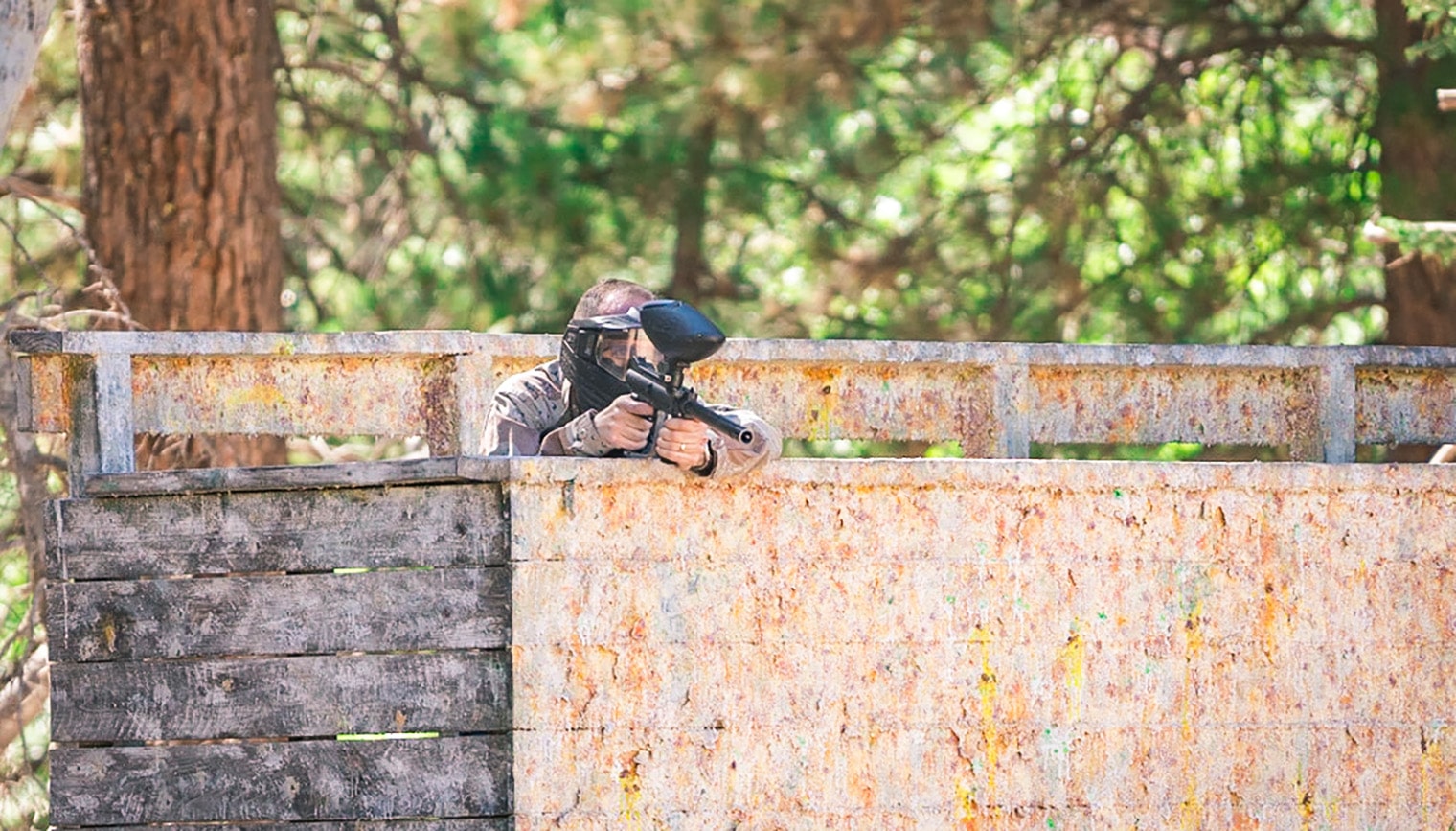 A person aiming a paintball gun from behind a barrier.