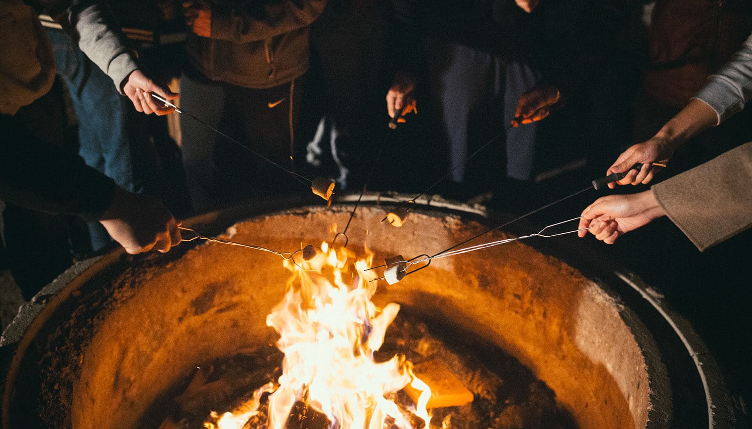 People toasting marshmallows around a camp fire.