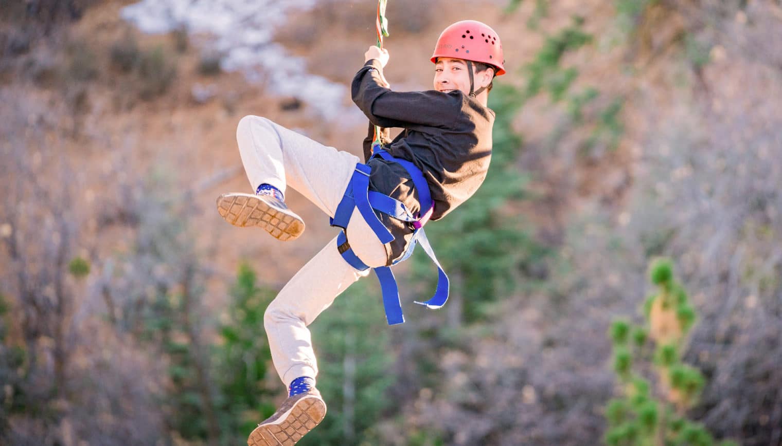 A person looking back and smiling as they ride a zip line.
