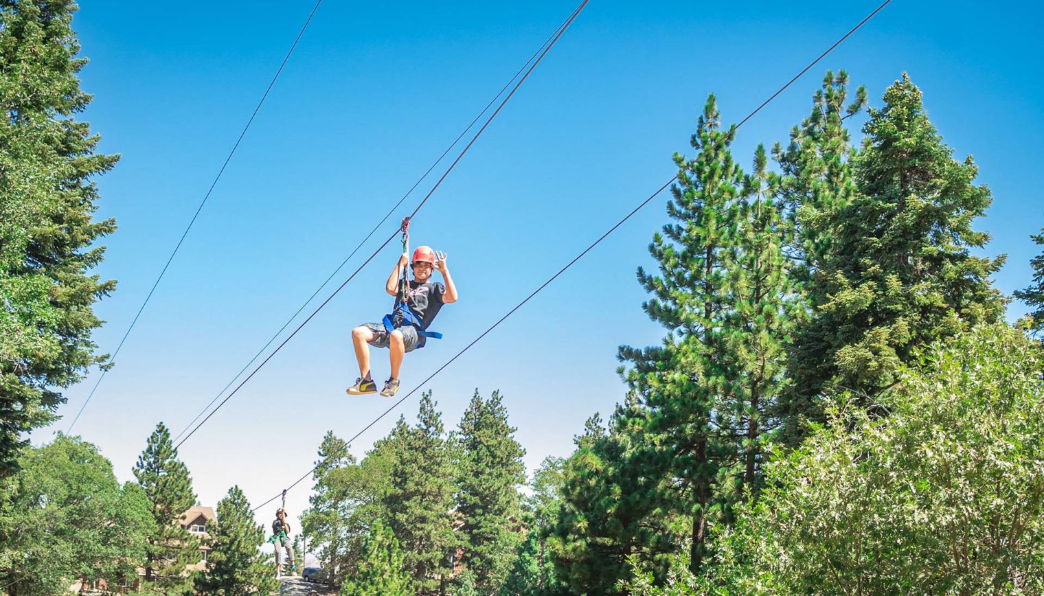 A person waving as they ride a zip line.