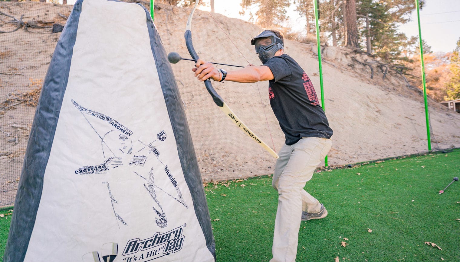 A person aiming a bow and arrow from behind an archery tag barrier.