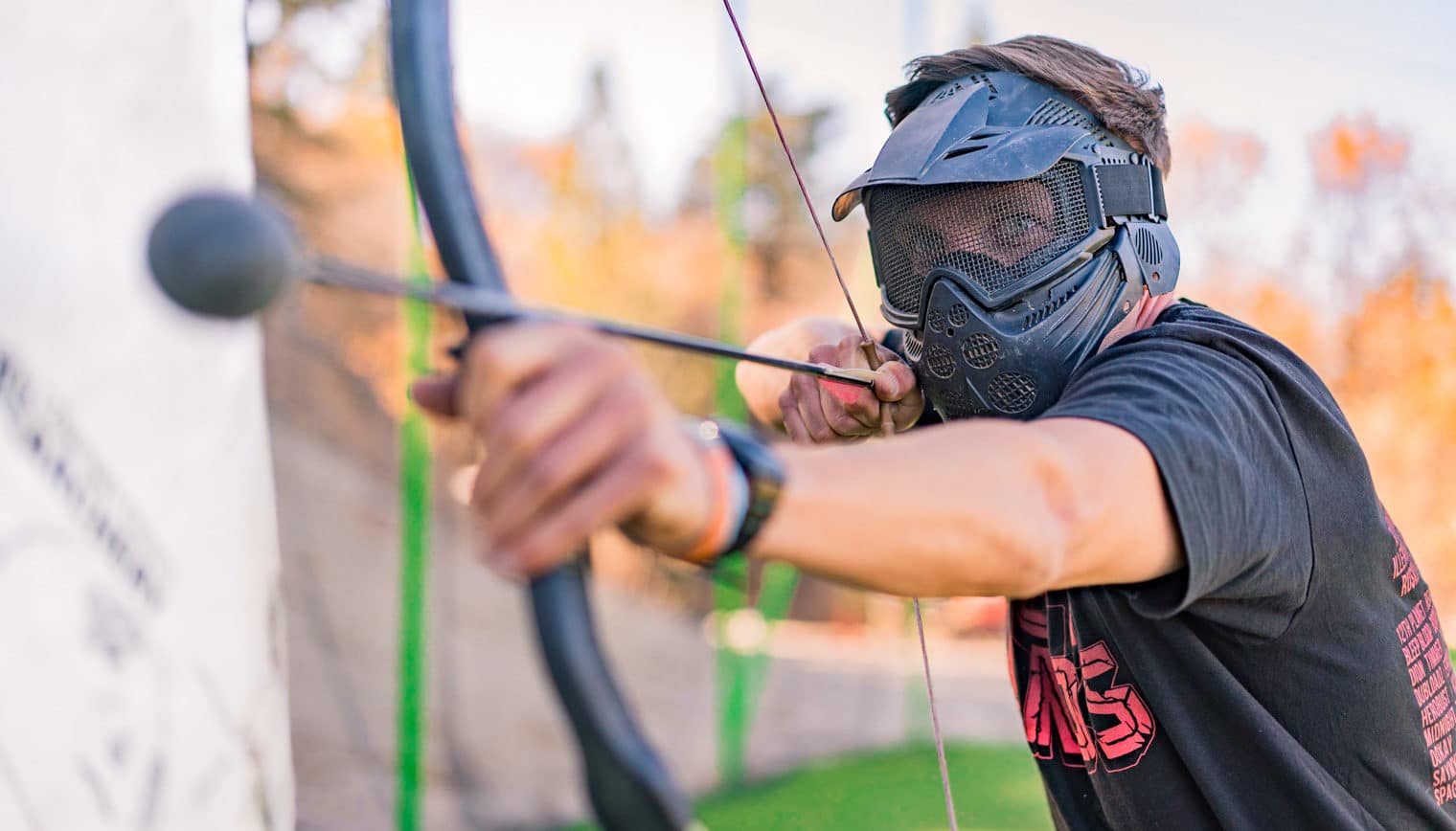 A man in archery tag gear, aiming a bow and arrow.
