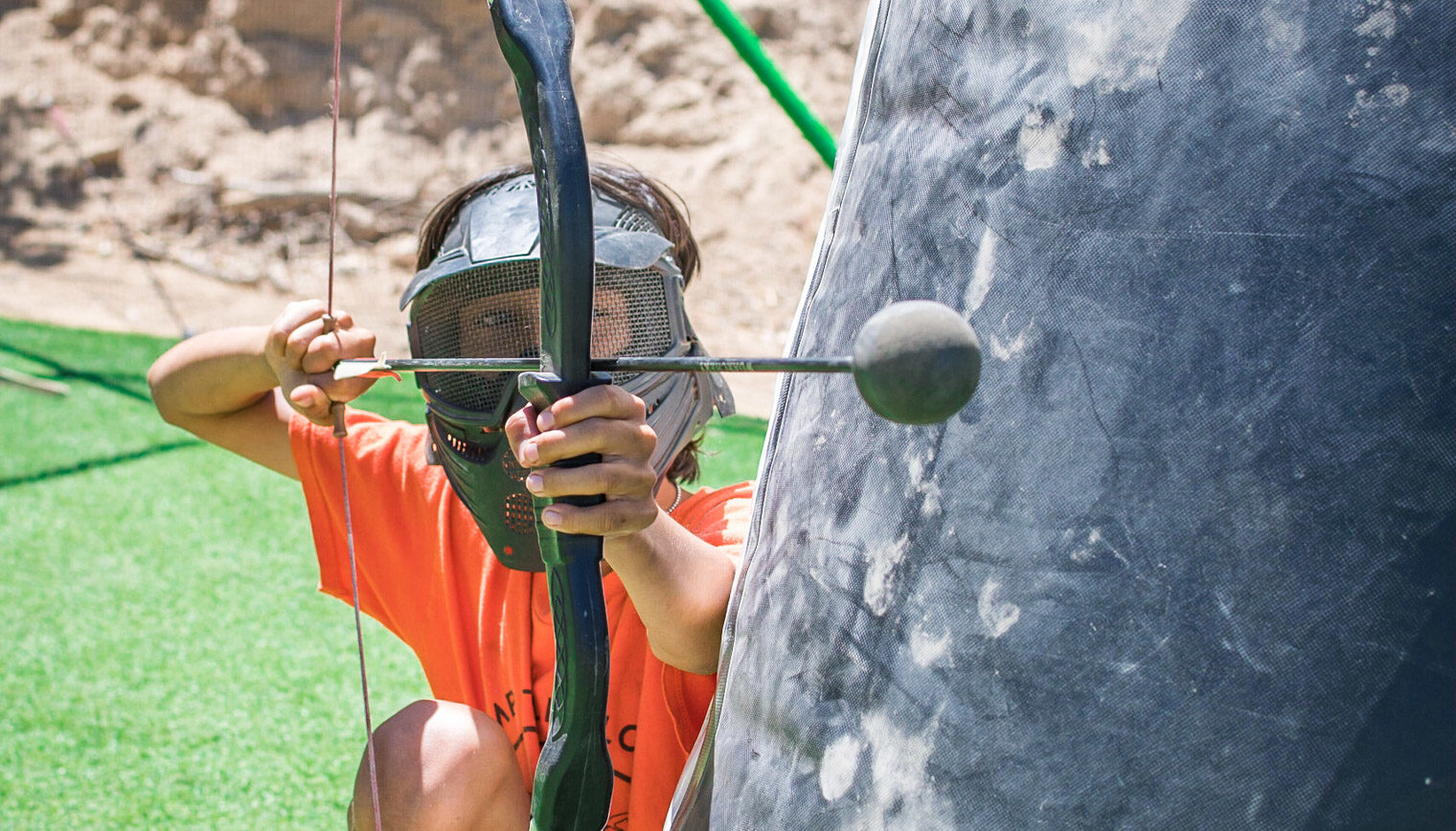 A person aiming a bow and arrow from behind a barrier.