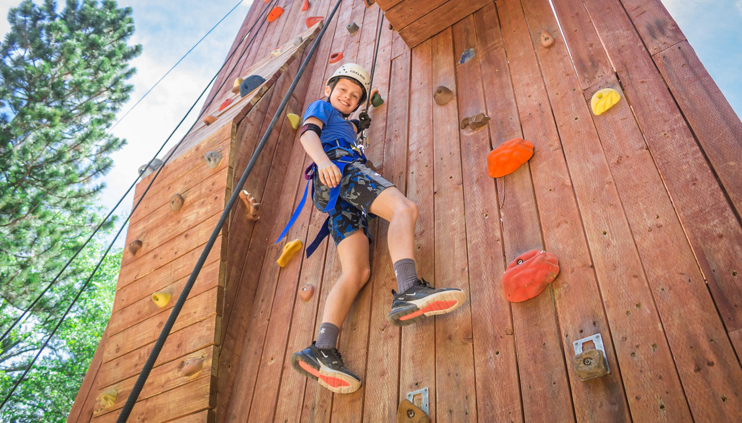 A boy smiling as he climbs a rockwall.