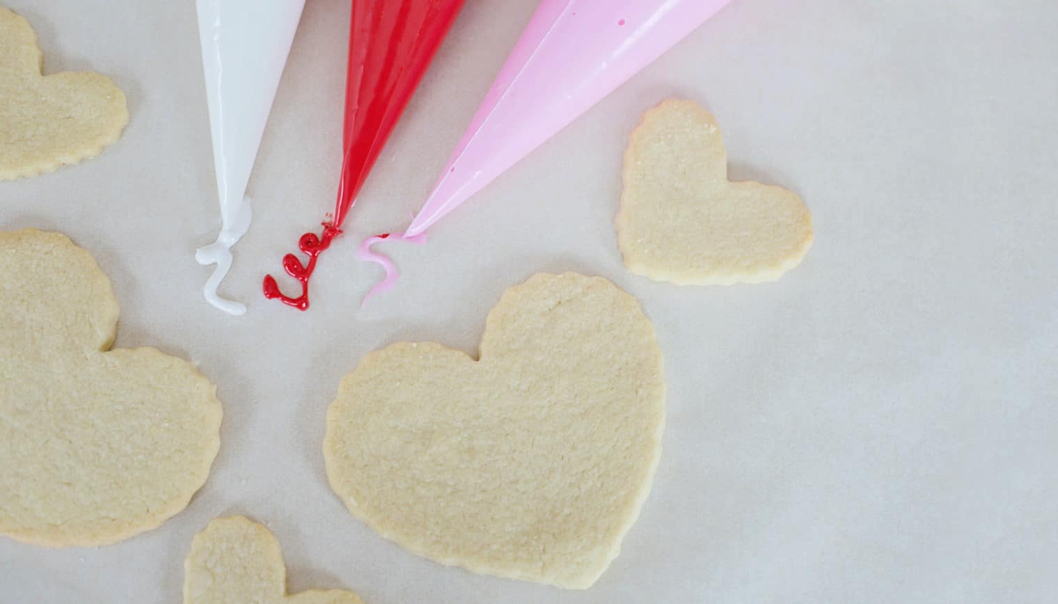 Heart shaped sugar cookies alongside three tubes of icing.
