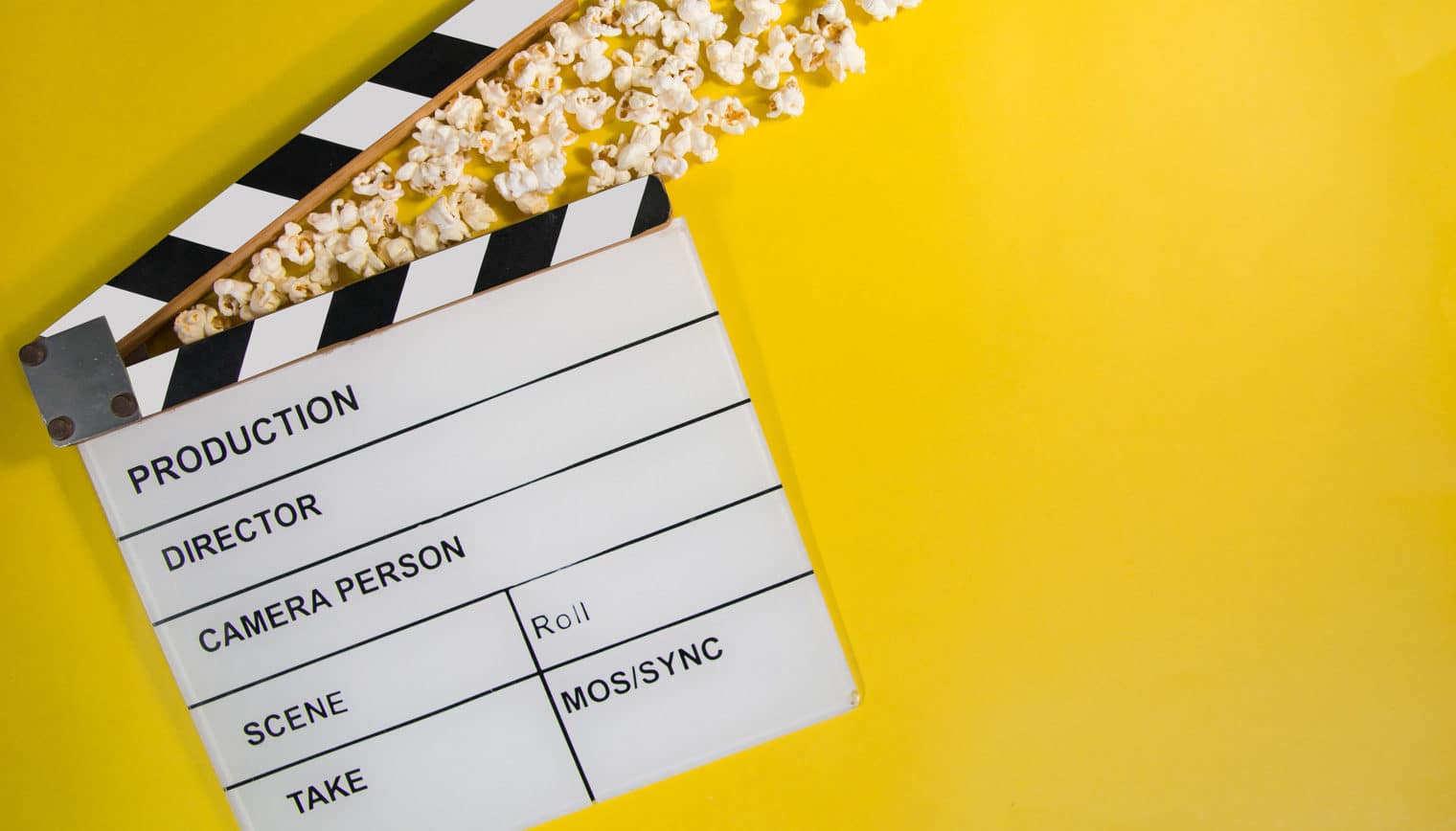 A film slate on a yellow background with popcorn.