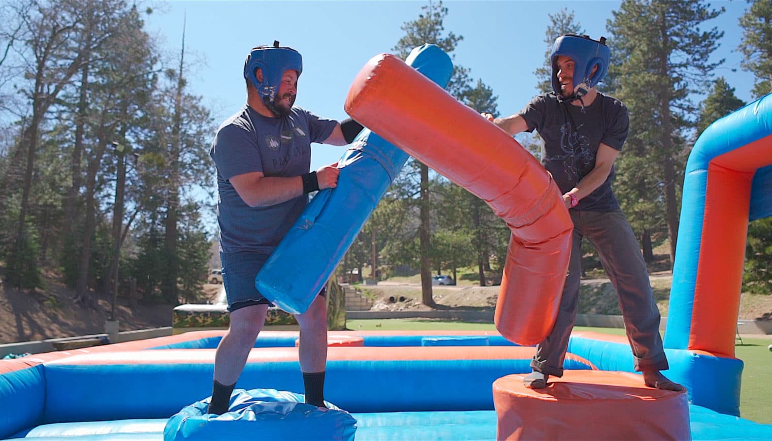 Two men jousting on a red and blue inflatable.
